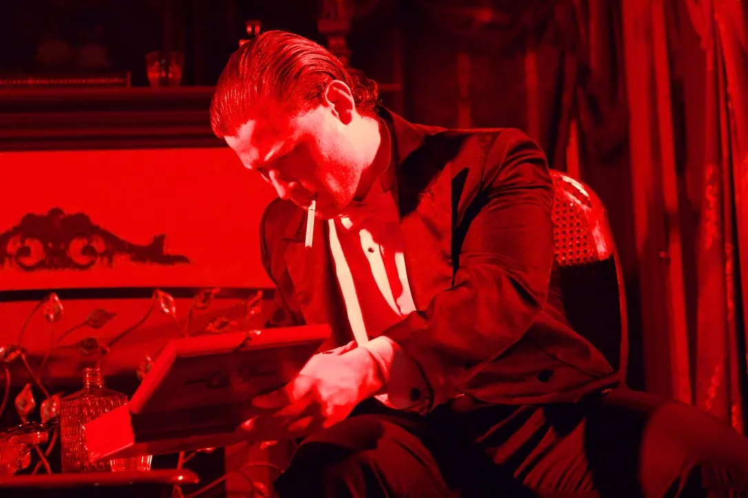 Nimrod Endvelt as Arthur Birling studying a book under red stage lighting
